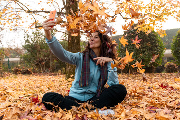 Woman sitting in fallen autumn leaves taking a selfie with her smartphone