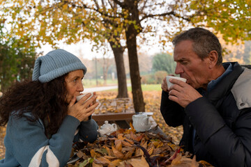 Senior couple sharing a cozy tea time outdoors amid colorful autumn leaves