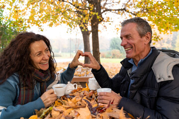 Happy senior couple making heart shape with hands during an autumn date in park