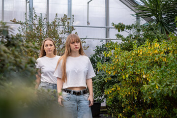 Mother and daughter standing together in a lush greenhouse, surrounded by vibrant greenery, showcasing their close relationship and shared moments of joy and connection