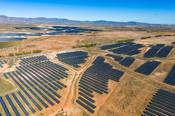 Sustainable Energy: Aerial View of a Massive Solar Farm Array Blanketing the Arid Landscape near...