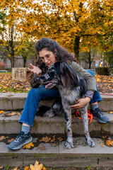 Woman sitting on stairs in park, affectionately interacting with her merle dog during autumn