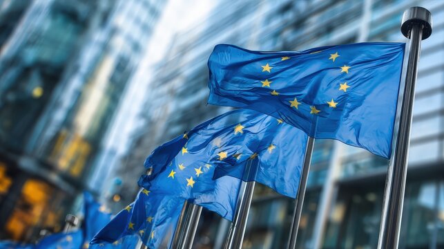 European Union flags flutter in the breeze against a backdrop of modern buildings, symbolizing unity and cooperation among member nations.