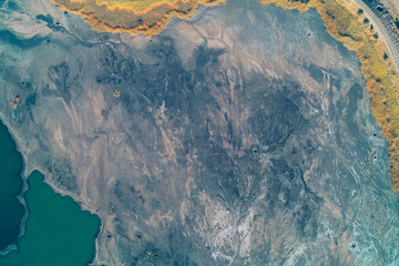 High-detail aerial abstract showing the intricate texture and flow patterns of dried blue-gray industrial tailings. Corner of vibrant emerald water provides a sharp, toxic color contrast and boundary.