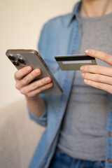 Vertical view of a woman holding a credit card and using a smartphone for online shopping, entering payment details for transaction on the internet, mobile banking. Close up.