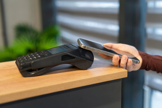 Pay by phone payment card reader. Closeup woman hand using smartphone cashless wallet NFC technology to pay order on bank terminal. Wireless Contactless payment in the store. Close-up