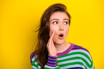 Surprised young brunette woman in colorful striped sweater on bright yellow background looks to the side with open mouth expression