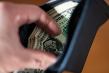 A blurred hand places or taking folded US dollar bills, with George Washington's portrait visible, into a dark wallet. Concepts of savings, payment, budget, and finance