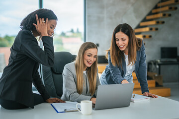 Diverse businesswomen collaborating on a laptop at a modern office