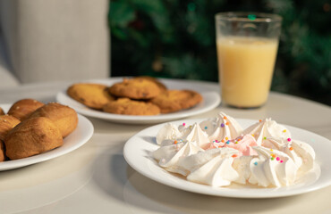 Colorful meringues with cookies and a glass of juice placed on a bright table, creating a cozy dessert scene.