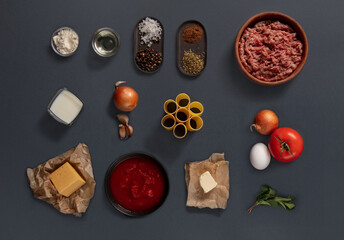 A variety of fresh ingredients are laid out for cooking, including ground meat, tomatoes, cheese, garlic, and spices. The items suggest preparation for a savory pasta recipe.