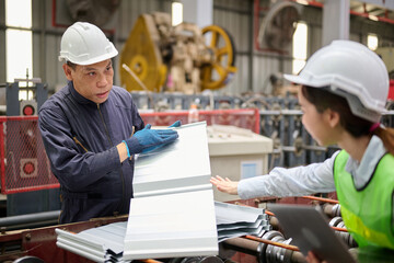 Workers reviewing metal sheet in a factory. They are focused on assessing a piece of metal, dressed in protective gear, surrounded by machinery
