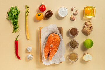 Fresh salmon fillet is placed on a wooden board surrounded by vibrant vegetables and spices, ready for preparation in a clean kitchen space.
