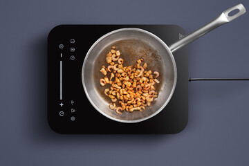 Shrimp are sizzling in a pan on an induction stove. A modern kitchen setting provides a sleek...