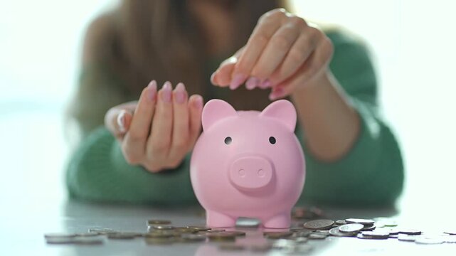 Woman budgeting for profit. Close up woman placing coins into piggy bank. Financial planning and budgeting concept. Woman managing finances to increase profit. Piggy bank symbolizes saving and profit.