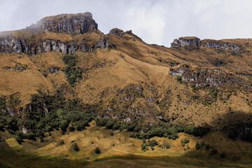 Imponente macizo andino en el Parque Nacional Natural Los Nevados, Colombia. Contraste dramático de luz y sombra sobre acantilados rocosos y laderas cubiertas de pastos secos. Texturas geológicas y be