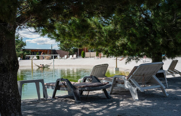 White deck chairs by the lake in the shade between coniferous trees