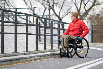 A man in a wheelchair wearing a red jacket moves along an asphalt path.