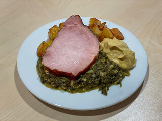 Traditional German winter dish featuring hearty Gruenkohl kale stew served with tender Kassler smoked pork, crispy fried potatoes, and mustard. Classic regional comfort food from Northern Germany.