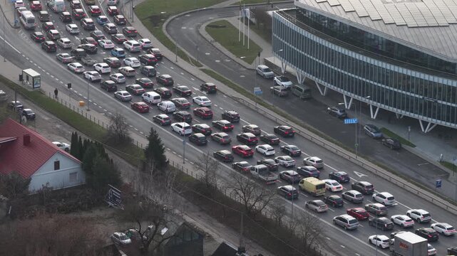 Aerial view of heavy traffic congestion on a multilane road in Vilnius, next to a contemporary glass-fronted office building during daytime rush hour.
