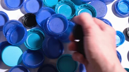 Human hand picking black plastic bottle caps from pile of blue lids in bright close up, waste sorting process, recycling education, eco initiatives and packaging industry visuals
