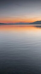 Fototapeta premium Calm lake at sunset with distant mountains and colorful sky.