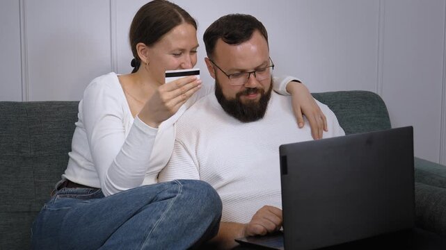Young couple sitting on couch and using world wide web for home shopping and using credit card and laptop to shop online