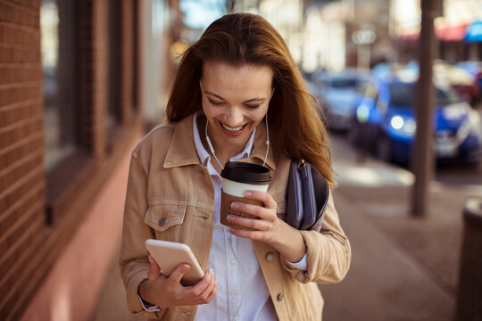 Young adult woman smiling with coffee and smartphone on city street