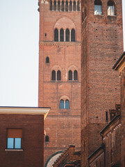 Torrazzo bell tower and adjacent old brick buildings forming a textured composition under clear sky, highlighting Italian heritage