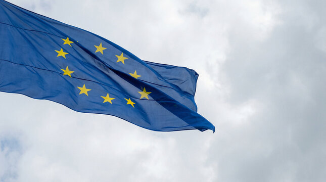 The European Union flag waves in the wind with a cloudy sky backdrop, symbolizing resilience. Ideal for thematic articles or presentations.