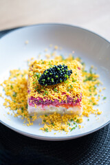 Close-up of a colorful layered salad topped with black caviar and garnished with finely chopped chives on a white plate.