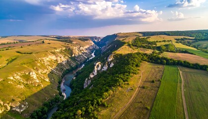 Aerial shot of a verdant river canyon cutting through rolling fields, bathed in warm sunlight and punctuated by white cliffs
