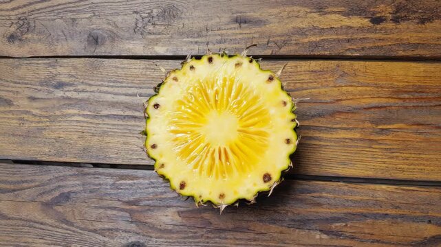 Fresh pineapple ring spinning on a rustic wood surface in a stop motion video sequence. Healthy tropical fruit ingredient for summer recipes or a detox diet concept