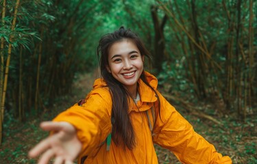 A pleasant young woman wearing an orange jacket is shown in this image of a bamboo forest hand stretching toward the camera while grinning.