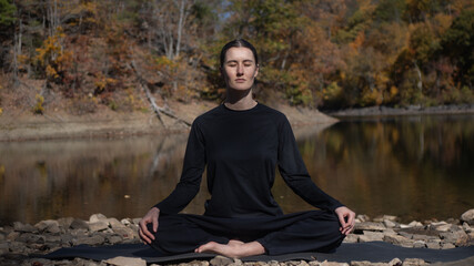 Woman meditating outdoors in autumn by riverbank with closed eyes