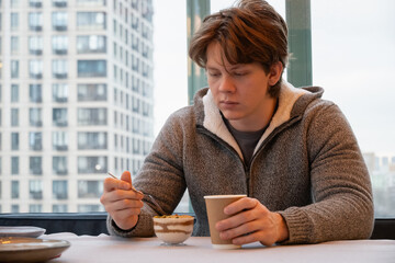 Young man sit and relax at cafe with coffee and dessert in bowl. Coffee break at modern city.