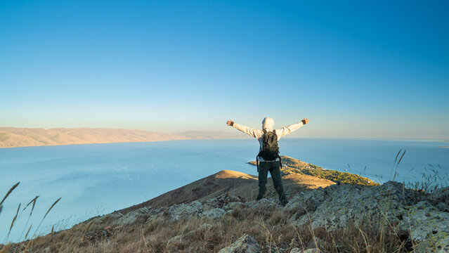 Traveler sitting with open arms on a rocky hill above Lake Sevan, Armenia, enjoying the freedom and beauty of nature with a wide blue horizon.
