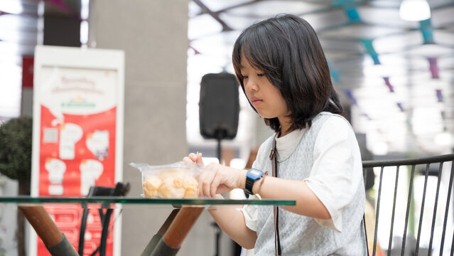 A girl opening a snack container while sitting at an outdoor cafe.