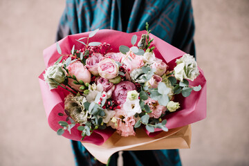Very nice young woman holding big and beautiful bouquet of fresh roses, eustoma, eucalyptus flowers in pink and white colors