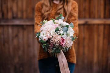 Very nice young woman holding big and beautiful wedding bouquet of fresh freesia, eucalyptus, roses, peonies flowers in pink and white colors