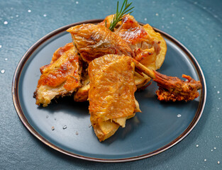 Roast chicken with crispy skin served with roasted potatoes and rosemary on a dark plate. High-detail food photography with natural lighting and clean composition