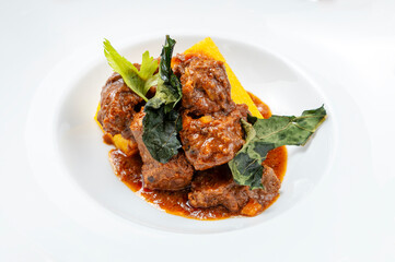 Stewed veal served with creamy polenta and finished with crispy greens in a rich red sauce. High-detail food photography with natural light and clean white plating