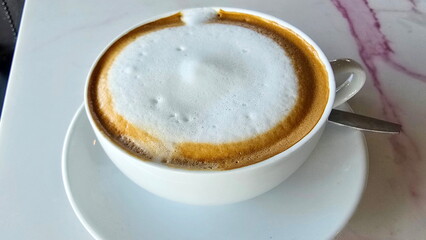 Top view of hot coffee cup with milk foam served on cream-colored coaster. Latte, cappuccino, mocha are caffeinated hot beverages. Popular drink the coffee flavor is not too strong. relieve drowsiness