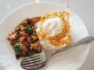 Stir-fried minced pork with basil and a fried egg on hot steamed rice served with a fork and spoon. A popular one-dish meal. Main course, quick meal. Stir-fried chili and pork with basil leaves.
