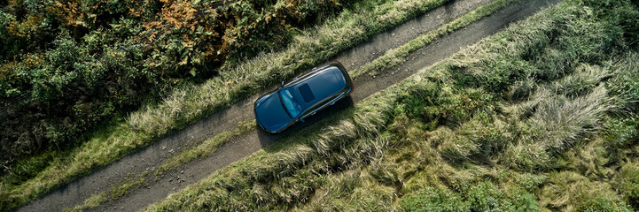A black vehicle navigates a narrow dirt road lined with vibrant greenery and splashes of autumn colors. The remote location showcases the beauty of nature and tranquility.