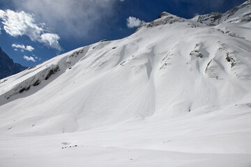A sunny view of the snow-covered slopes and mountain peaks in the Annapurna Sanctuary, Himalayas, Nepal. The sky is blue with scattered white clouds
