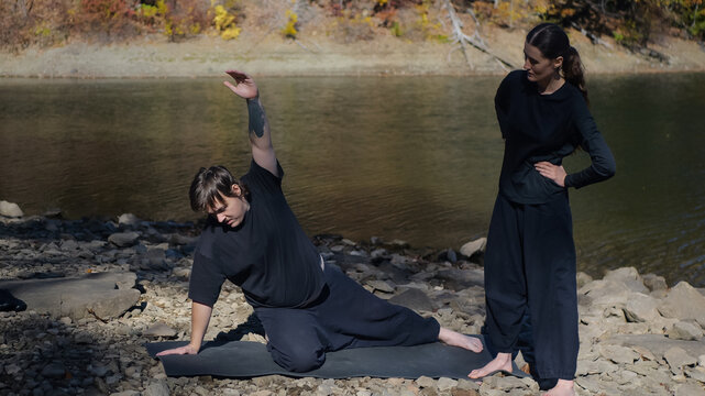 Outdoor yoga session by a lake with instructor observing