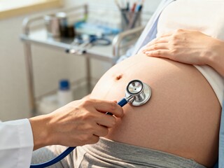 Healthcare professional checking a pregnant woman's belly with a stethoscope during a prenatal checkup, focusing on fetal health.