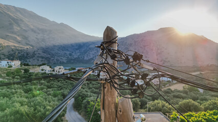 Chaotic wires on old pole with Cretan nature background, outdated electricity transmission method