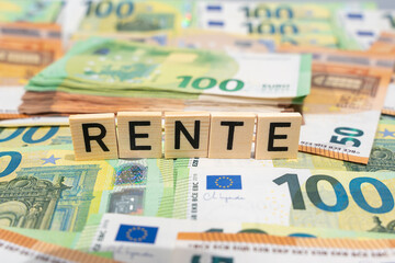 Wooden tiles spell Rente in front of stacked euro banknotes. Shallow depth of field illustrates retirement income and financial planning.